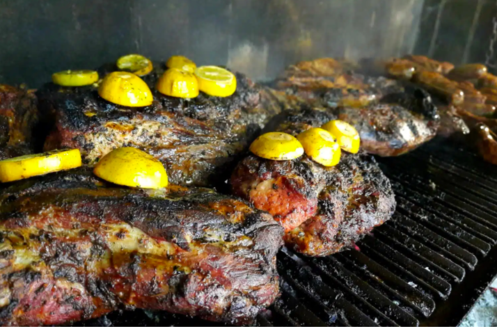 Traditional Argentine asado meats grilling over open flames with fresh lemon.