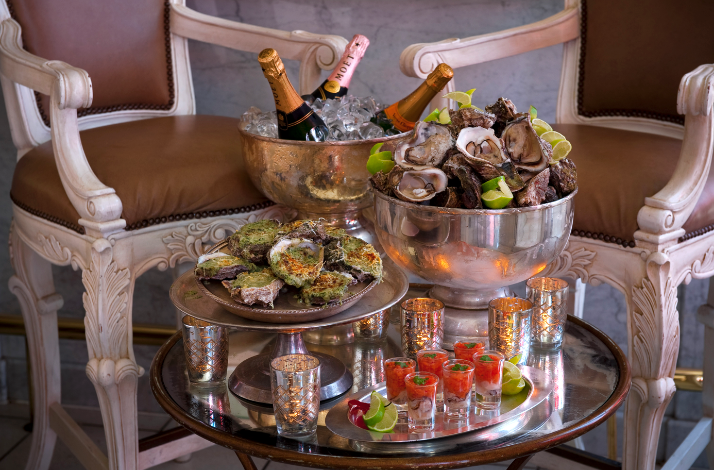 Seafood and champagne spread with oysters, canapés, and drinks on a small table.