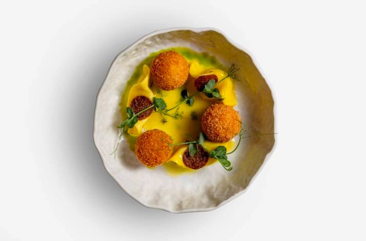 Golden fried croquettes arranged on a yellow sauce with micro herb garnishes, served in a textured white ceramic bowl at Restaurant Lemongarden.