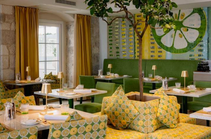 Sun-drenched interior of Restaurant Lemongarden, Sutivan, with citrus-themed decor, set marble tables, gold lamps, and stone-wall accents.