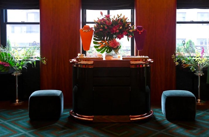 Ornate necklaces on velvet busts atop a curved Art Deco bar, surrounded by tropical blooms in Casa Cruz New York's interior.