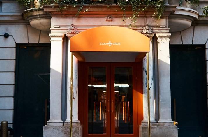 Casa Cruz New York entrance featuring an orange arched awning with 'Casa Cruz' signage above brass-framed orange doors.