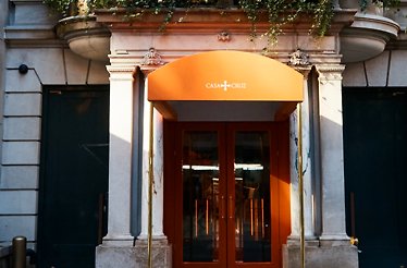 Casa Cruz New York entrance featuring an orange arched awning with 'Casa Cruz' signage above brass-framed orange doors.