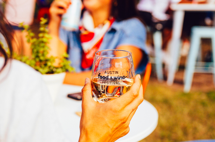 A guest holding a glass of water with the Austin Food and Wine Festival logo.