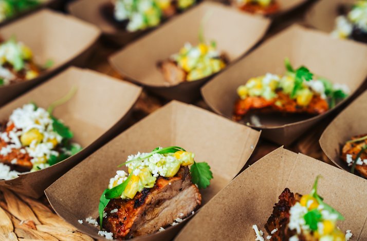 Rows of small cardboard trays holding grilled meat topped with corn salsa, crumbled cheese, and fresh herbs, served at Austin Food and Wine Festival.