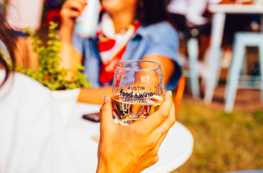 A guest holding a glass of water with the Austin Food and Wine Festival logo.
