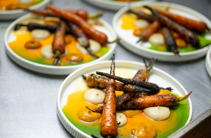 Multiple plates ready to serve (charred carrots with sauces; vibrant colors).