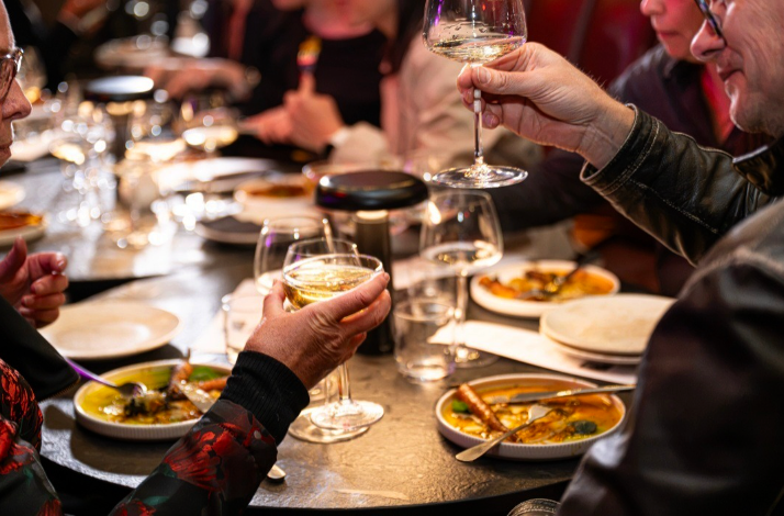 Guests toasting with white wine around a shared table.