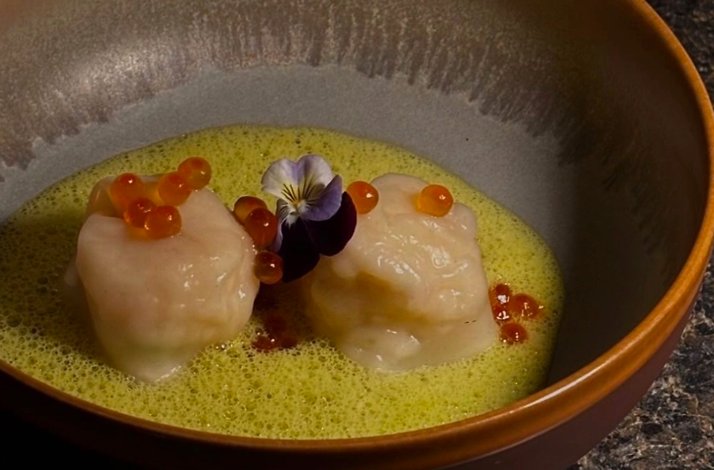 Zitz Sum course featuring steamed dumplings adorned with trout roe and an edible pansy in a bright herb broth.