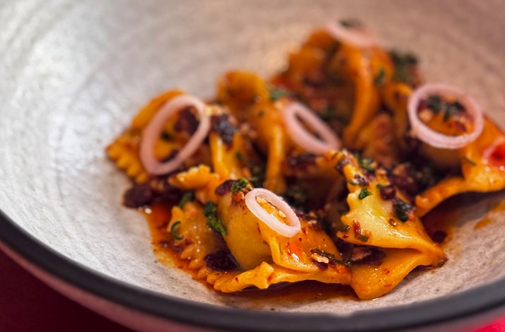 Braised dumplings in rich spiced broth, garnished with pickled shallot rings and fresh herbs, served at Zitz Sum.