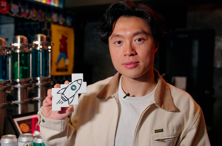 Mr. Mahjong holding four mahjong tiles that form a rocket drawing.