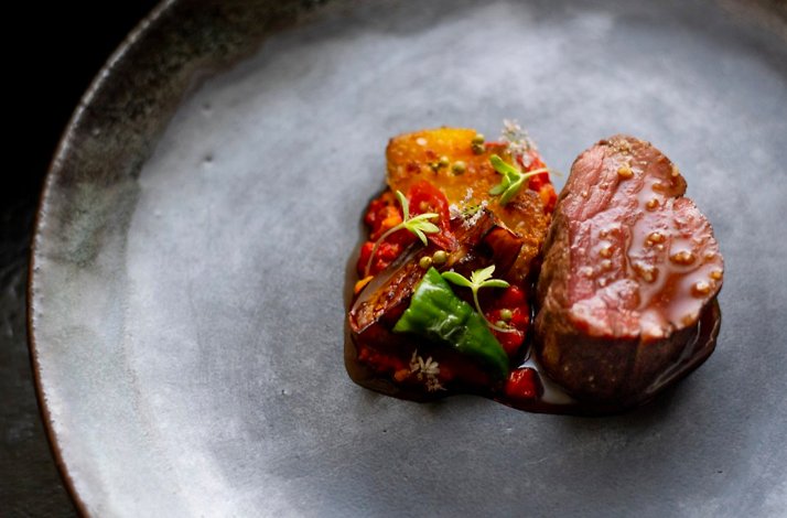 Medium-rare sliced meat medallions plated beside roasted peppers, eggplant, and herb garnish on a matte grey ceramic plate at Nightbird.