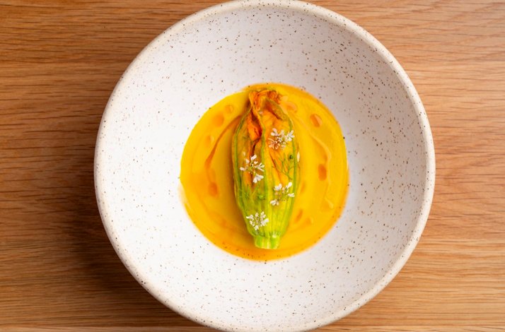 Stuffed zucchini blossom resting in vibrant golden sauce, garnished with tiny white flowers, served at Jacaranda.