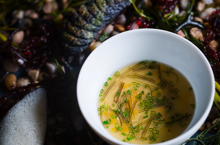 Chef Michael Cimarusti's mussel broth served in a white bowl, nestled among seaweed and pebbles at Providence.