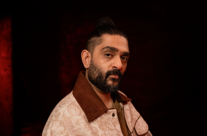 Singer Sid Sriram looking at the camera against a dark red background.