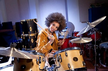 Acclaimed jazz and rock drummer Cindy Blackman Santana smiling while holding drumsticks behind a full drum kit.