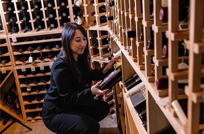 Sommelier Valentina Crescimanni retrieving a labeled wine bottle from an extensive cellar storage wall at A'Cuncuma, Palermo.