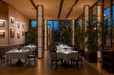 Golden Blitz restaurant interior in Bucharest at dusk, featuring illuminated columns, white-clothed tables, and framed wall art.