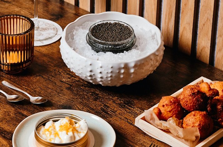 Elegant caviar presentation on ice with fried fritters and whipped cream accompaniment on a rustic wooden table at Little Water.