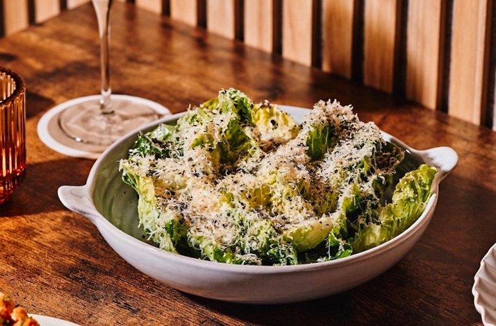 Crisp romaine salad mounded with shaved parmesan in a two-handled stoneware bowl on a warm wooden table at Little Water.