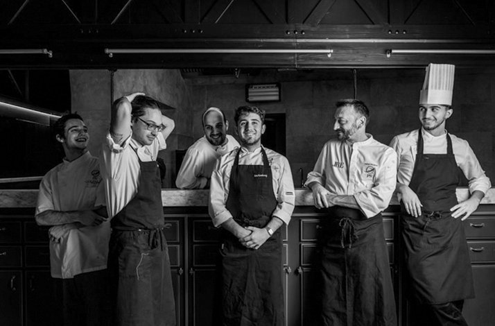 Chef Stefano Pinciaroli and five kitchen team members laughing together in Ps Ristorante’s kitchen.
