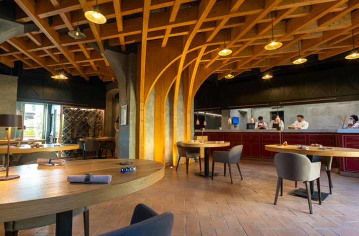 Spacious Ps Ristorante interior with arched wooden ceiling, round tables, and open kitchen staffed by chefs.