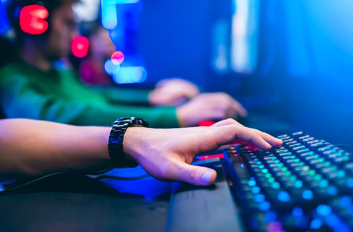 Gamer playing on an illuminated RGB keyboard in a blue-lit gaming arena.