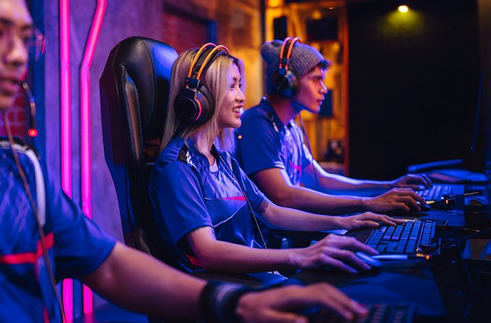 Smiling female gamer with a headset playing alongside teammates in a neon-lit esports arena.