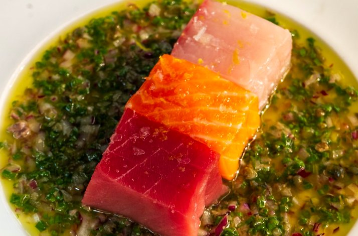 Three cubes of raw fish on herb vinaigrette in a white bow, served at Prime Seafood Palace.