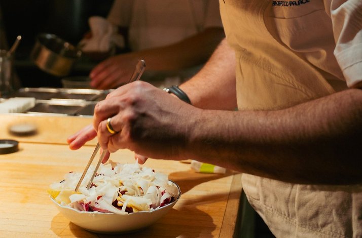 A Prime Seafood Palace Chef plating a salad at a wooden counter.