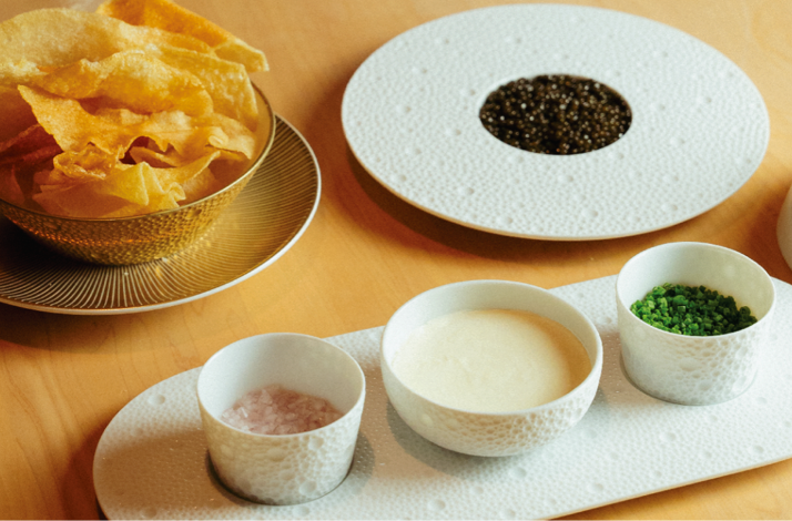 Caviar service with potato chips, crème fraîche, chives, and salt on a table. Served at Prime Seafood Palace.