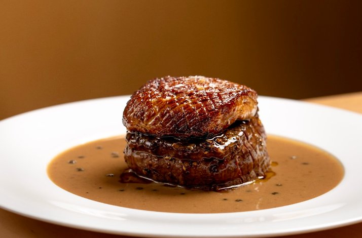Seared beef medallion topped with foie gras in peppercorn sauce on a white plate, served at Prime Seafood Palace.