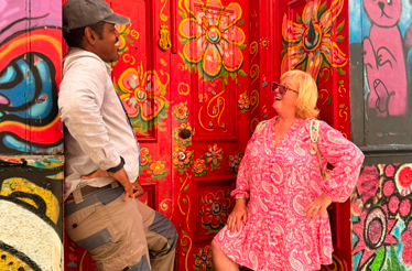 A guest and a local resident chat in front of a vividly painted doorway surrounded by colorful street art in Valparaíso.
