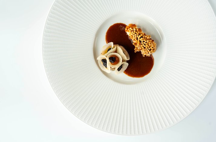 Plated fine-dining dish at Restaurant Fris: crisp garnish and dark sauce on a large white patterned plate.