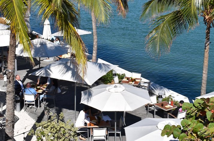 Waterfront dining patio at Amara at Paraiso with white umbrellas and palm trees.
