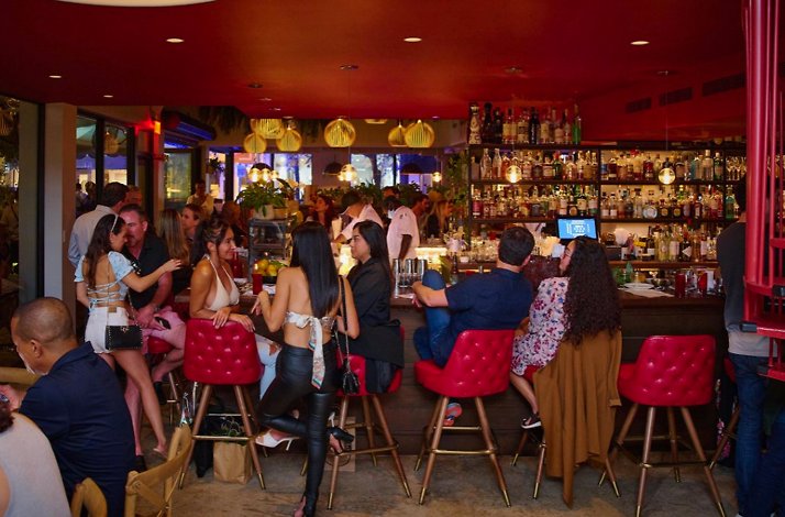Lively bar scene at Michael's Genuine Food & Drink, with guests gathered around red-accented bar seating beneath warm pendant lights.