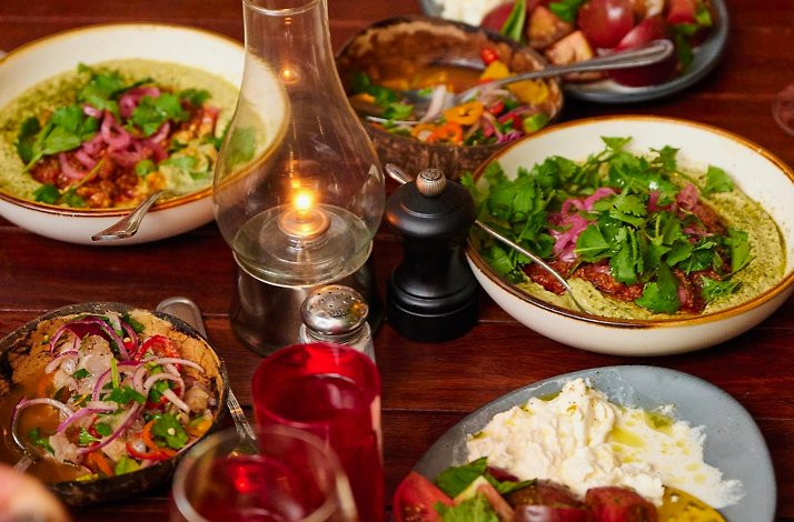 Multiple herb-garnished seasonal dishes sharing a candlelit wooden table at Michael's Genuine Food & Drink, Miami.
