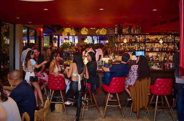 Lively bar scene at Michael's Genuine Food & Drink, with guests gathered around red-accented bar seating beneath warm pendant lights.