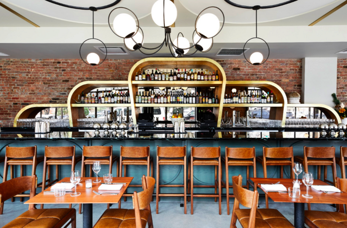 Warm-toned interior at Ernesto's with a curved gold bar, globe pendant lighting, and set dining tables.