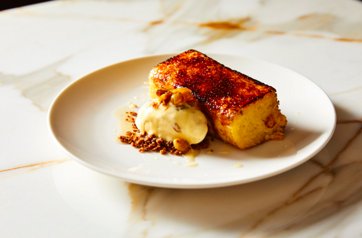 Caramelized golden-crusted dessert slice served with cream and crushed nuts on a white plate at Ernesto's.