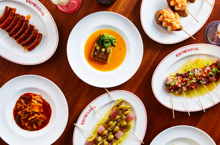 Variety of Ernesto's signature Basque-inspired dishes arranged on a wooden table, including skewers and stewed plates.