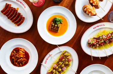 Variety of Ernesto's signature Basque-inspired dishes arranged on a wooden table, including skewers and stewed plates.