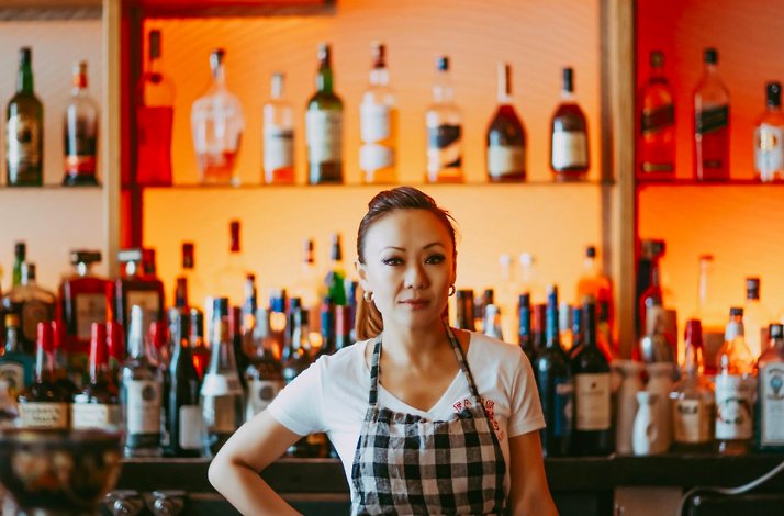 Chef Kathy Fang standing in front of the fully stocked cocktail bar counter at Fang Restaurant.