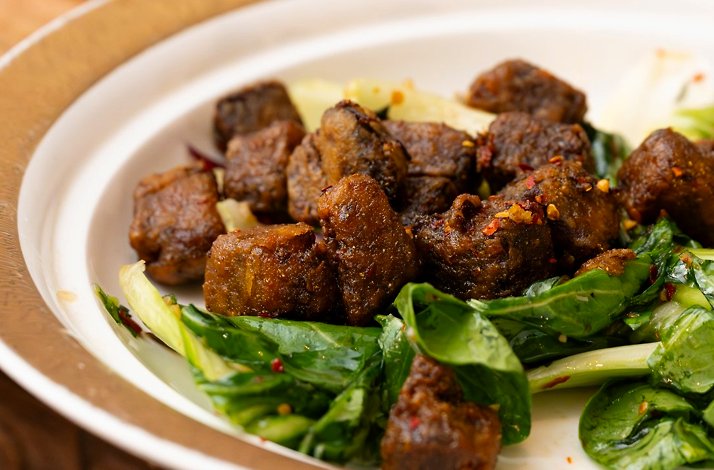 Stir-fried beef short ribs served over bok choy greens on a white rimmed plate at Fang Restaurant.