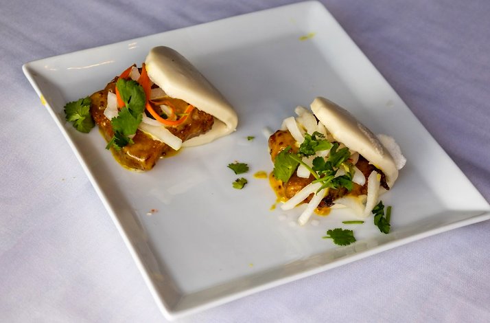 Two pork belly bao buns topped with cilantro and pickled vegetables on a white plate at Fang Restaurant.