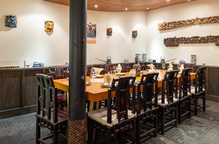 A long wooden table set for group dining in a private room decorated with colorful masks at Fang Restaurant.