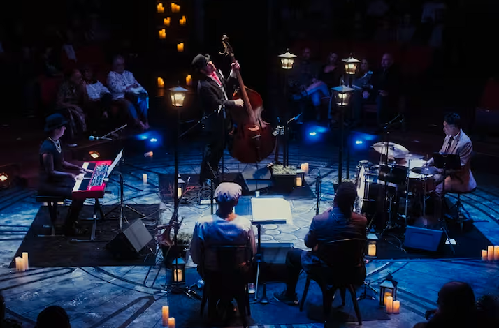 A live jazz band performing in an intimate, dimly lit circle venue decorated with streetlamps and candles.