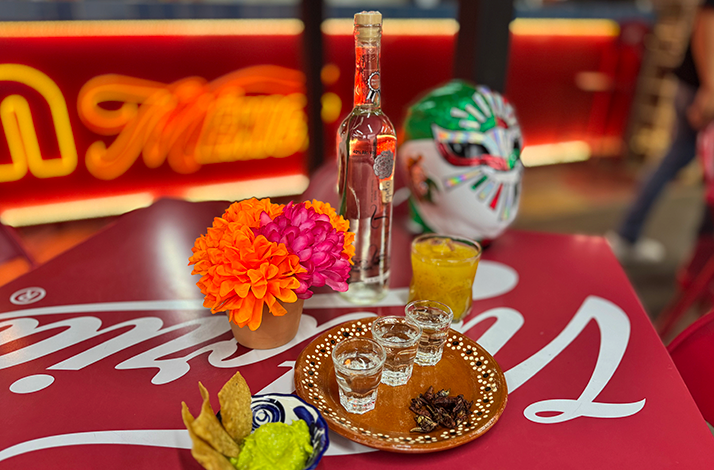 Traditional Mexican spirits, cocktails, snacks, and a lucha libre mask displayed on a table as part of a cultural tasting experience.