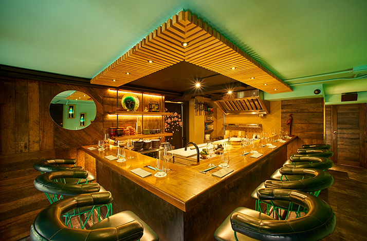 Exclusive chef's table inside a restaurant kitchen, featuring an intimate counter surrounding the sushi preparation area where guests can observe culinary techniques up close.