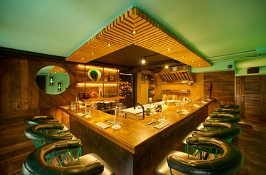 Exclusive chef's table inside a restaurant kitchen, featuring an intimate counter surrounding the sushi preparation area where guests can observe culinary techniques up close.